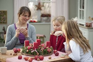 Mutter mit Töchtern bastelt Adventskranz