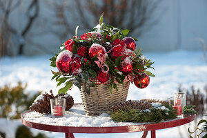 Weihnachtsstrauß mit roten Kugeln auf verschneitem Gartentisch