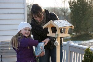 Mother and daughter filling a bird feeder