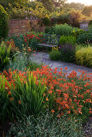 Ein Platz zum Sitzen - Metallsitz und Blick über Lanhydrock Garden mit Crocosmia 'Constance' und Erysimum 'Apricot Delight' im Vordergrund