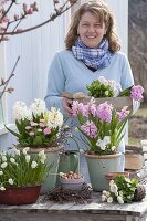 Frau arrangiert rosa-weißen Frühlings-Tisch auf der Terrasse