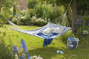 Suspended hammock between trees, bed with perennials and grasses