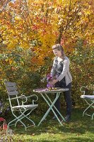 Small seating area with bouquet of asters in front of ironwood tree and ornamental apples