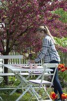 weiße Sitzgruppe unter Malus 'Scarlet' (Zierapfel) mit roten Blüten