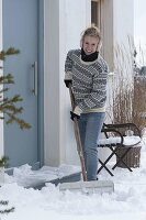 Frau schippt Schnee auf der Terrasse