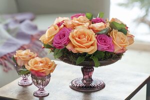 Gesteck aus Rosa (Rosen) mit Moos in flacher Schale mit Fuß und Gläschen