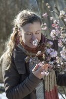 Frau schnuppert an bluehendem Zweig von Viburnum bodnantense 'Dawn'