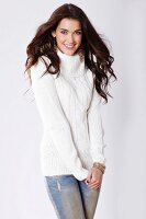 A brunette woman wearing a white cable-knit jumper and jeans