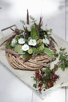 Wreath decorated with white asters, thistles and poppy seedheads next to posy of rose hips