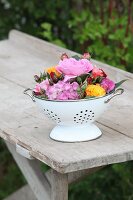 Hydrangeas and roses in shades of red and orange in vintage-style colander