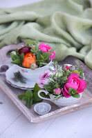 Bunte Blumengestecke in nostalgischen Tassen auf Vintage Holztablett