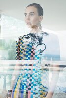 A brunette woman wearing a brightly coloured patterned dress standing behind a window pane