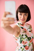 Junge brünette Frau in geblümtem Kleid macht ein Selfie mit ihrem Smartphone