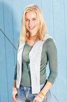 Blonde Frau in grünem Strick-Shirt, grauem Pullover über den Schultern und Jeans