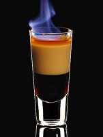 A flambéed B-52 cocktail in a glass on a black background