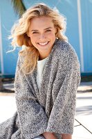 A young blonde woman in a white top and a grey mottled knitted cardigan