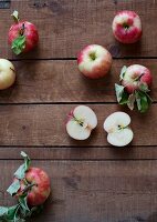 Frische Äpfel, ganz und halbiert, auf Holzuntergrund