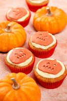 Several Pumpkin pie cupcakes shown with real pumpkins on a light orange background