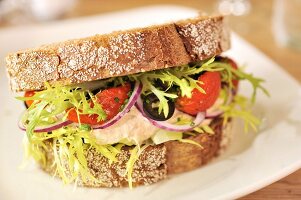 Sandwich mit Makrelenmayonnaise, getrockneten Tomaten, Oliven, roten Zwiebeln und Salat