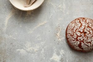 A baking tin and a baked loaf of bread on a flour-dusted worktop