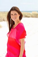 A brunette woman wearing a pink tunic on the beach