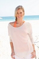 Blonde Frau in orangefarbenem Top und weißem Langarmshirt am Strand