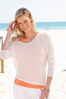 Blonde Frau in orangefarbenem Top und weißem Langarmshirt am Strand