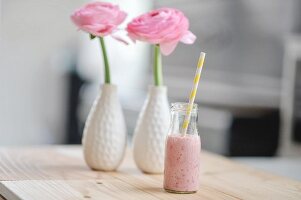 Raspberry milk with a straw in a bottle and pink ranunculus flowers in two vases