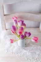 Pink and purple tulips in jug on lace doily on white chair
