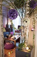 Elegant arrangements of artificial flowers, fairy lights and glass vases on grey plinths in front of living area with lit tealights