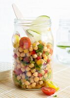 A chickpea salad in a glass jar with tomatoes, peppers, red onions, spring onions, spices, limes, olive oil and fresh parsley