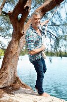 A man with grey hair wearing a checked shirt and jeans and holding onto a rope