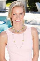 A blonde woman wearing a pink dress and a necklace in front of a pool