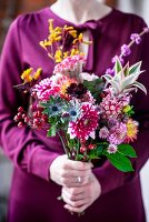 Frau hält Blumenstrauss in leuchtenden Herbstfarben in den Händen