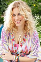 Woman with blonde curly hair wearing colourful tunic and eye-catching jewellery