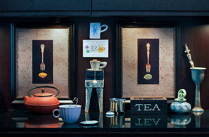 Teekanne und Tasse vor zwei beleuchteten Bildern mit Gabeln