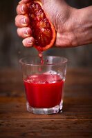 Blood orange being squeezed out by hand over a glass