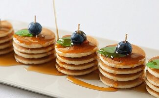 Several piles of mini pancakes with maple syrup, blueberries and mint