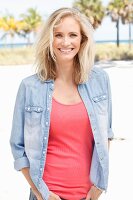 A blonde woman wearing a pink top and denim shirt