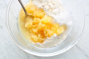 Tinned pineapple, baking powder, sugar and flour being mixed together in a bowl