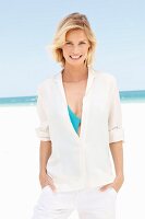 A blonde woman wearing a white blouse and white trousers on the beach