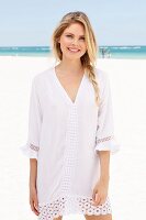A blonde woman wearing a white tunic dress with lace on the beach
