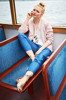 A blonde woman wearing a pink jacket, a white top, jeans and gold sandals