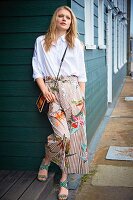 A blonde woman wearing a white oversized shirt, culottes with floral print, a shoulder bag and sandals