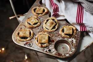 Six mince pies in a vintage baking tin with cream and red linen cloth on rustic white painted wooden chair