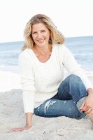 A blonde woman wearing a white jumper and jeans