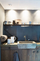 Stone sink below cups on shelf in rustic country-house kitchen