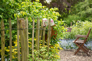 Staketenzaun aus Kastanienholz, im Hintergrund Gartenstühle auf Kiesfläche