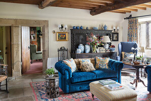 Scatter cushions on blue sofa and antique dresser in rustic living room wit wood-beamed ceiling