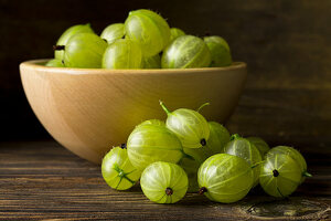 Green gooseberies in a wooden bowl and in front of it